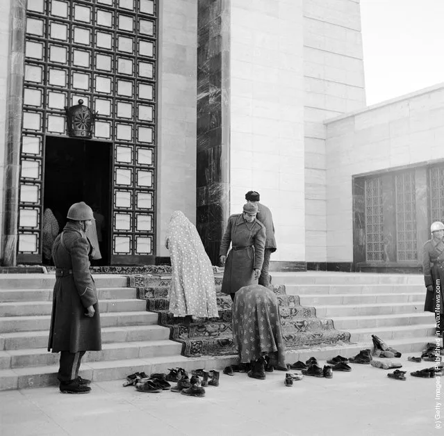 1950:  A woman taking off her shoes and leaving them with a pile of others at the entrance to the former Shah of Persia's Mausoleum which is guarded by soldiers