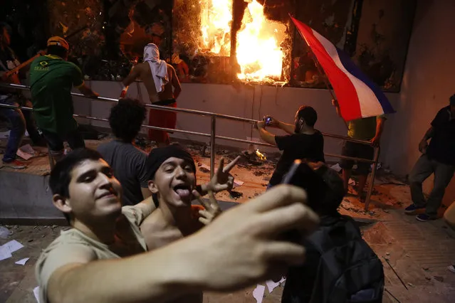 Men pose for a photo outside the congress building during clashes between police and protesters opposing an approved proposed constitutional amendment that would allow the election of a president to a second term, in Asuncion, Paraguay, Friday, March 31, 2017. Some protesters broke through police lines and entered the first floor, where they set fire to papers and furniture. Police used water cannon and fired rubber bullets to drive demonstrators away from the building while firefighters extinguished blazes inside. (Photo by Jorge Saenz/AP Photo)