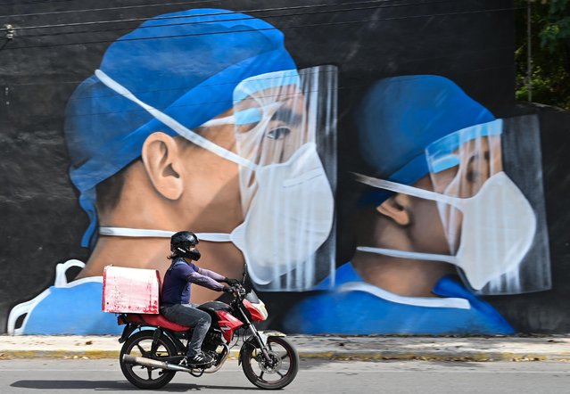 A motorcyclist drives past a mural of medical workers wearing face masks painted in the center of Merida by Mexican artists Mare Nookie on Sunday, January 23, 2022, in Merida, Yucatan, Mexico. (Photo by Artur Widak/NurPhoto via Getty Images)