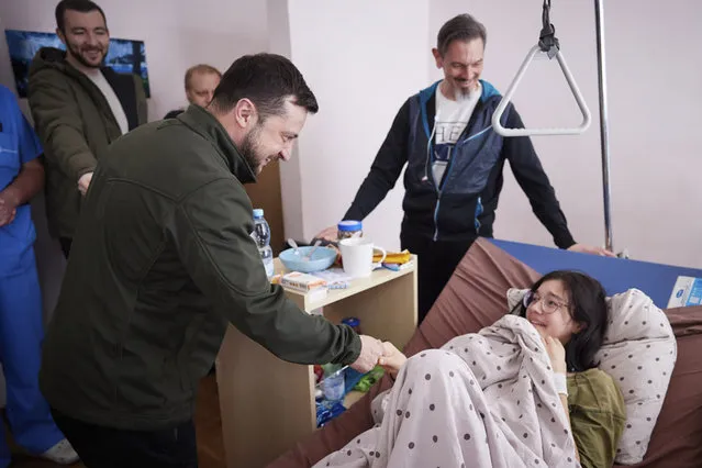 In this photo provided by the Ukrainian Presidential Press Office on Thursday, March 17, 2022, President Volodymyr Zelenskyy, shakes hands with a wounded Kateryna Vlasenko, 16, a refugee from Vorzel who covered her junior brother with her body during Russian shelling as they ran from their home town in a hospital in Kyiv, Ukraine. (Photo by Ukrainian Presidential Press Office via AP Photo)