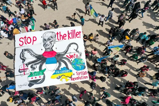 This picture taken on April 1, 2022 shows an aerial view of a giant sign being raised by protesters depicting Russia's President Vladimir Putin as an octopus with its arms wrapping around the countries of Georgia, Syria, Ukraine, and the world globe during demonstration in the city of Binnish in Syria's northwestern rebel-held Idlib province against Russia's invasion of Ukraine. (Photo by Omar Haj Kadour/AFP Photo)