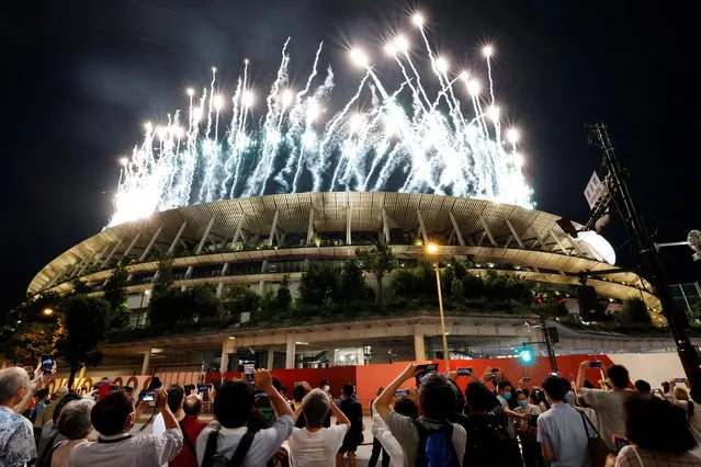 People take photos outside as fireworks light up the sky above the Olympic Stadium during the opening ceremony for the Tokyo 2020 Paralympic Games in Tokyo on August 24, 2021. (Photo by Issei Kato/Reuters)