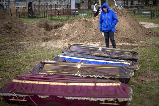 Ira Slepchenko, 54, cries next to coffins, one of them with the body of her husband Sasha Nedolezhko, 43, during an exhumation of civilians killed and buried in a mass grave in Mykulychi, Ukraine on Sunday, April 17, 2022. All four bodies in the village grave were killed on the same street, on the same day. Their temporary caskets were together in a grave. On Sunday, two weeks after the soldiers disappeared, volunteers dug them up one by one to be taken to a morgue for investigation. (Photo by Emilio Morenatti/AP Photo)
