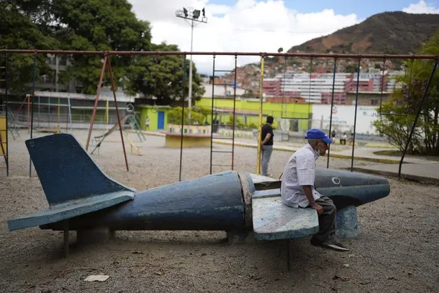 An elderly man sits on a plane made of cement at a park near a soup kitchen as he waits to pick up his free lunch in Caracas, Venezuela, Friday, March 11, 2022. Venezuela has just over five million pensioners, according to official figures, but annual inflation which reached 686.4% last year has eaten up their pensions. (Photo by Ariana Cubillos/AP Photo)