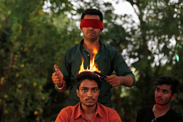 Vishnu Limbachiya, a hair artist, styles the hair of a man while wearing a blindfold at a park in Ahmedabad, India, May 31, 2017. (Photo by Amit Dave/Reuters)