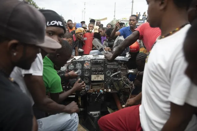 Onlookers play with the instrument panel of a small plane that crashed in the community of Carrefour, Port-au-Prince, Haiti, Wednesday, April 20, 2022. (Photo by Joseph Odelyn/AP Photo)