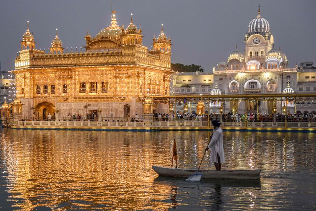 A Sikh Sewadar (volunteer) rows a boat at the holy sarovar or sacred pool on the backdrop of illuminated Golden temple on the birth anniversary of Guru Angad Dev Ji, the second guru of Sikhs, in Amritsar on May 1, 2022. (Photo by Narinder Nanu/AFP Photo)