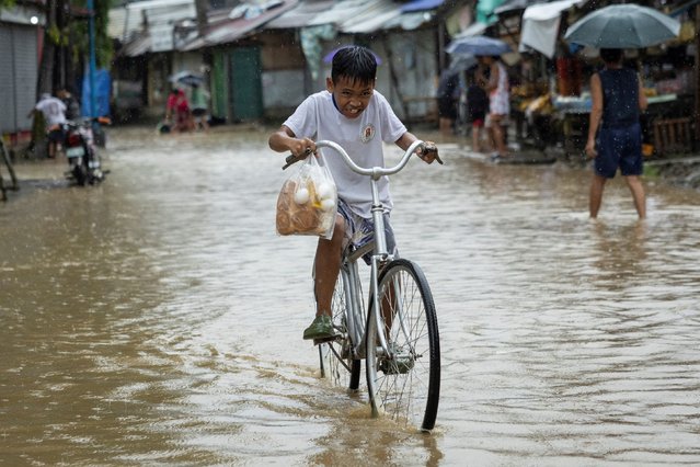 A boy carrying a plastic bag with bread and eggs, rides his bike through a flooded road after heavy rains brought by Tropical storm Yagi, locally known as Enteng, in Baras, Rizal province, Philippines, on September 2, 2024. (Photo by Eloisa Lopez/Reuters)