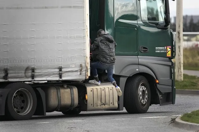 A migrant jumps on a truck in Calais, northern France, Thursday, October 14, 2021, to cross the tunnel heading to Britain.  In a dangerous and potentially deadly practice, he is trying to get through the heavily policed tunnel linking the two countries by hiding on a truck. (Photo by Christophe Ena/AP Photo)
