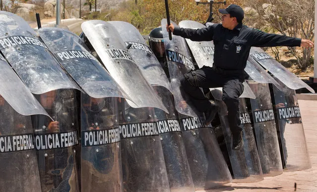 A Mexican Federal Police instructor jumpds on the plastic shields of a riot squad forming a barrier in Cabo San Lucas, Baja California, Mexico, at an undisclosed temporary base