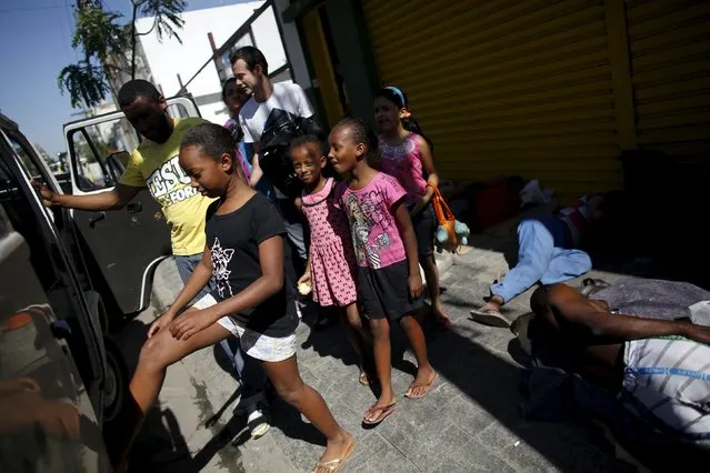 Young girls board a van taking them to ballet lessons at the New Dreams dance studio, as people sleep on the street in the Luz neighborhood known to locals as Cracolandia (Crackland) in Sao Paulo, Brazil, August 14, 2015. For the young girls learning to jump and plie, the dance studio provides a way forward and out of the difficult environment they have grown up in. (Photo by Nacho Doce/Reuters)