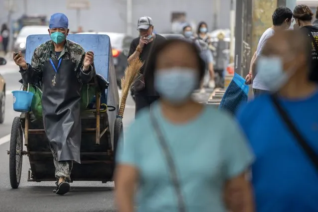 A maintenance worker wearing a face mask pulls a cart along a street in Beijing, Wednesday, July 6, 2022. (Photo by Mark Schiefelbein/AP Photo)
