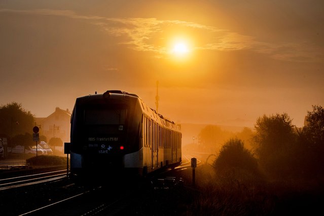 A regional train approaches the station in Wehrheim near Frankfurt, Germany, as the sun rises on a foggy morning, Tuesday, September 3, 2024. (Photo by Michael Probst/AP Photo)