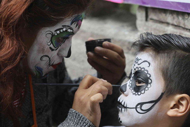A woman applies makeup to a youth at Mexico's annual Catrinas parade, ahead the Day of the Dead, in Mexico City, Sunday, October 27, 2024. (Photo by Ginnette Riquelme/AP Photo)