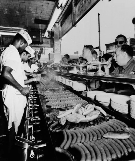 In this September 10, 1958 file photo, hot dogs are cooked on the grill as customers line up at at Nathan's Famous in Coney Island in the Brooklyn borough of New York. For decades, the showmen behind the annual Nathan's Famous hot dog eating contest on the 4th of July have been telling reporters the tradition began in 1916 with a showdown between patriotic immigrants on the Coney Island boardwalk. That would make this Monday, July 4, 2016 contest a centennial, of sorts, except for an inconvenient truth: the backstory was invented in the 1970s by PR men trying to get the hot dog stand on the map. (Photo by AP Photo)