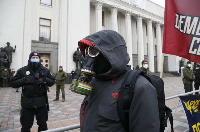 A protester in a gas mask takes part in a rally in front of the parliament building in Kyiv, Ukraine, Tuesday, March 17, 2020. Protesters demanded lawmakers to stop working amid nation-wide quarantine in order to prevent hastily adopting unpopular laws. In an additional set of measures preventing the spread of the new coronarivus, Ukrainian authorities ruled to close public places except food markets, pharmacies and gas stations starting from Tuesday in Kyiv and other regions, and restrict the use of public transport from Kyiv to other Ukrainian cities. (Photo by Efrem Lukatsky/AP Photo)