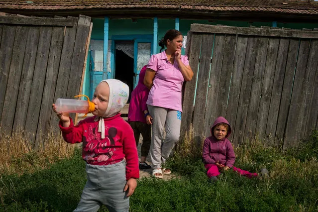 A family waits outside a house without electricity for volunteers to install a solar panel on their house, July 24, 2017, in the village of Gorbanesti, in northeastern Romania. For five years now the Light For Romania project have been bringing power into some of the lowest- income homes in the European Union' s second poorest nation. (Photo by Andrei Pungovschi/AFP Photo)