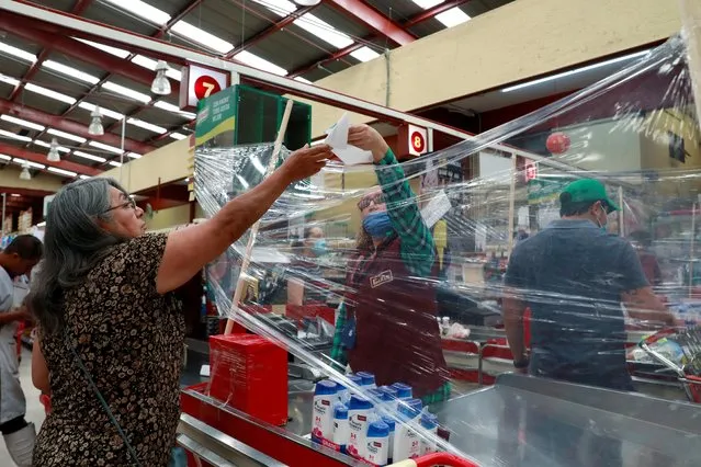 A cashier serves customer behind a makeshift plastic barrier as a preventive measure against the spread of the coronavirus disease (COVID-19) at Garis supermarket in Toluca, Mexico on March 28, 2020. (Photo by Henry Romero/Reuters)