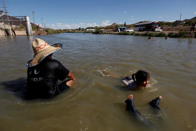 People sit in the Rio Bravo to cool off during a hot summer day on the Mexican side of the river near the fence marking the border between Mexico and the U.S in Ciudad Juarez, Mexico, July 24, 2016. (Photo by Jose Luis Gonzalez/Reuters)
