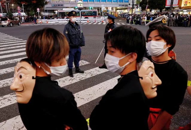 Revellers dressed in costumes wait in front of a crosswalk as policemen are in position to control crowds gathering to celebrate Halloween on the street at Tokyo's Shibuya entertainment and shopping district in Tokyo, Japan on October 31, 2022. (Photo by Kim Kyung-Hoon/Reuters)