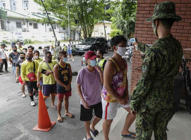 Men who were arrested for violating quarantine health protocols have their temperatures checked at the Amoranto Sports Complex in Manila, Philippines on Wednesday, July 8, 2020. Philippine President Rodrigo Duterte eased one of the world's longest lockdowns in the Philippine capital of more than 13 million people on June 1 after the economy shrank in the first quarter in its first contraction in more than two decades. (Photo by Aaron Favila/AP Photo)