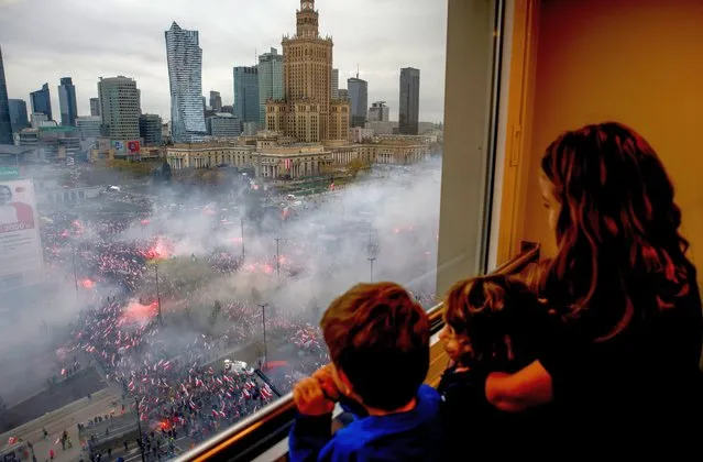 Children watch from a window as thousands of people have gathered in the city center for a yearly Independence Day march organized by nationalist groups that has been marked by violence in past years in Warsaw, Poland, Friday, November 11, 2022. (Photo by Michal Dyjuk/AP Photo)