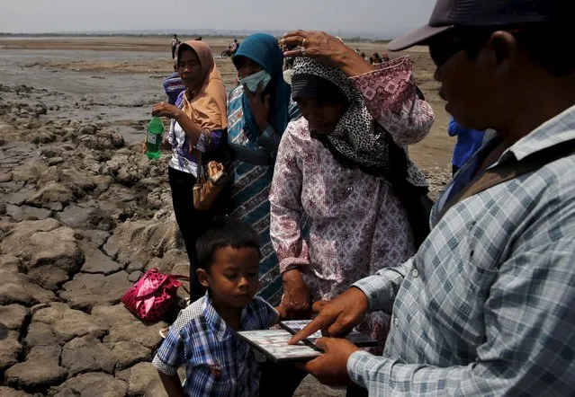 A villager (R) sells videos of the mudflow disaster to tourists at the Lapindo mud field in Sidoarjo, October 11, 2015. (Photo by Reuters/Beawiharta)