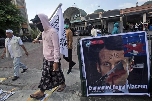 Muslim men walk past a defaced poster of French President Emmanuel Macron during a protest at Al Jihad mosque in Medan, North Sumatra, Indonesia, Friday, October 30, 2020. Muslims around the world have been calling for both protests and a boycott of French goods in response to France's stance on caricatures of Islam's most revered prophet. (Photo by Binsar Bakkara/AP Photo)