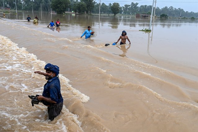 Residents wade through a flooded area of Kartarpur, a town in Punjab province, on August 28, 2025. Pakistan authorities blew up an embankment next to a monsoon-engorged dam on August 27 as flooding submerged one of the world's holiest Sikh sites. Three transboundary rivers in the east of the country have swollen to exceptionally high levels as a result of heavy rains across the border in India. (Photo by Arif Ali/AFP Photo)