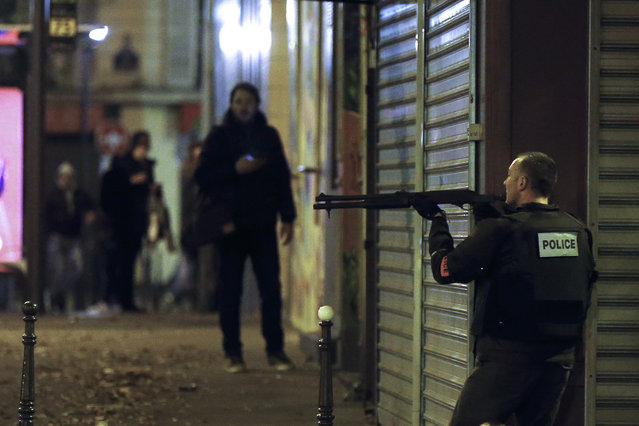 A French police officer takes cover while on the lookout for the shooters who attacked the restaurant 'Le Petit Cambodge' earlier tonight in Paris, France, November 13, 2015. (Photo by Etienne Laurent/EPA)