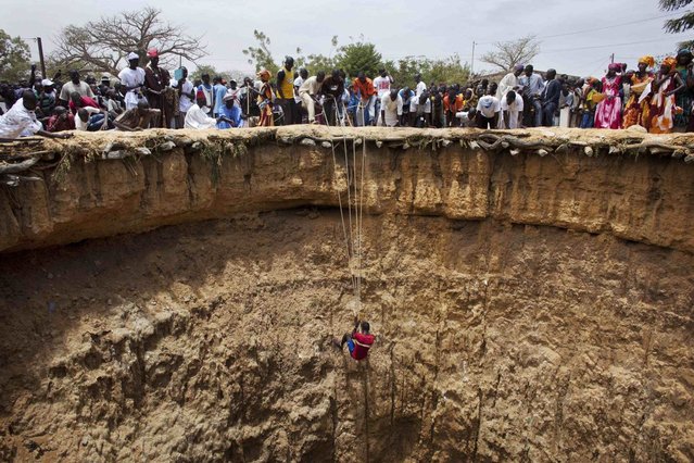 People watch a man descend into a large former well during a traditional ceremony in the village of Ndande, May 19, 2013. Every year, inhabitants of the village take part in a Sufi Muslim ceremony called Gamou-Ndande. The ceremony combines nights of praying and chanting as well as traditionally animist ceremonies. The well, called Kalom, was the site of historic battles in Senegalese history. According to local historian Baye Niass, the well dates back to the 16th century. Today there is no water in the former well and it is used for ceremonial purposes. Niass says the well measure 36 meters in depth an 11m in diameter. (Photo by Joe Penney/Reuters)