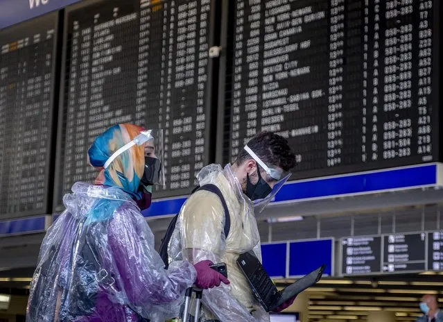 Passengers with protection gear walk past the flight board at the airport in Frankfurt, Germany, Friday, July 24, 2020. (Photo by Michael Probst/AP Photo)