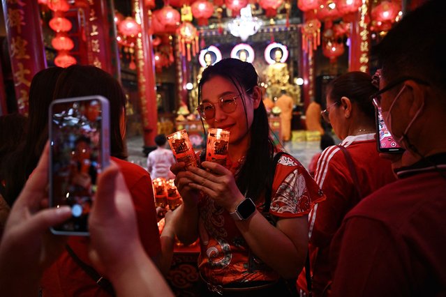 A woman poses for photos with lit candles at a shrine on the first day of the Lunar New Year of the Snake in Bangkok on January 29, 2025. Hundreds of millions of people across Asia celebrate the Lunar New Year with their families on January 29, as they bid farewell to the Year of the Dragon and usher in the Year of the Snake. (Photo by Lillian Suwanrumpha/AFP Photo)