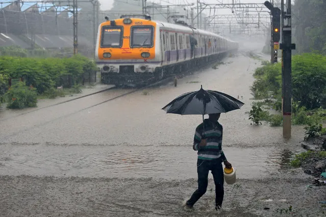 A man carrying an umbrella walks past a passenger train that moves through a water-logged track during heavy rains in Mumbai, India, July 9, 2018. (Photo by Francis Mascarenhas/Reuters)