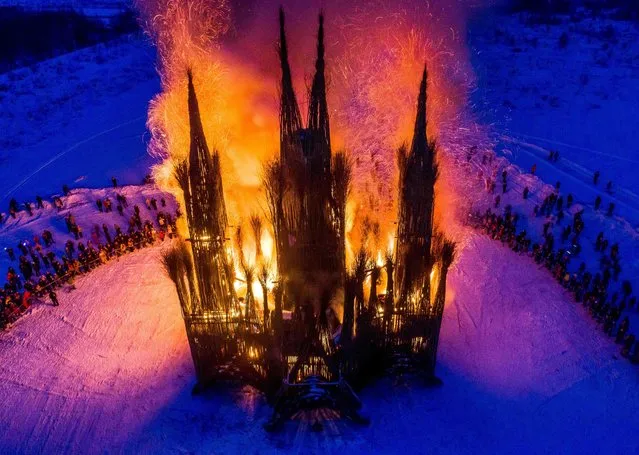 An aerial view taken with a drone on February 17, 2018 shows spectators as they watch the burning of a thirty- meter structure built of twigs and debris made in the form of a Gothic style building by Russian artist Nikolay Polissky during the celebration of Shrovetide (Maslenitsa) in the village of Nikola- Lenivets, Kaluga region, some 220 km (140 miles) outside Moscow.  Shrovetide or Maslenitsa is an ancient farewell ceremony to winter, traditionally celebrated in Belarus, Russia and Ukraine and involves the burning of a large effigy. German Vinogradov, performance artist at Nikola- Lenivets, turned the huge art object into an openwork burning building, according to organizers. (Photo by Dmitry Serebryakov/AFP Photo)