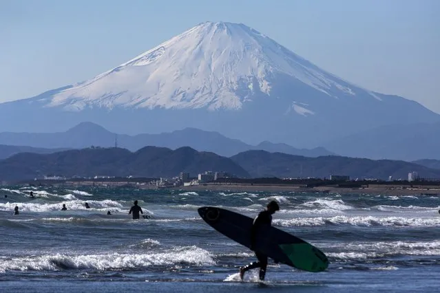 A surfer walks off to the beach as Mount Fuji is viewed in the background Friday, February 19, 2021, in Fujisawa, west of Tokyo. (Photo by Kiichiro Sato/AP Photo)