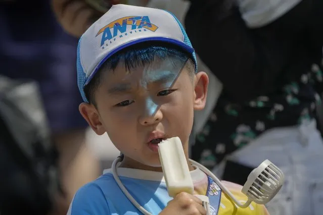 A boy wearing an electric fan eats an ice cream near the Forbidden City on a sweltering day in Beijing, Friday, July 7, 2023. (Photo by Andy Wong/AP Photo)