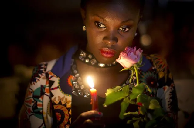 A Kenyan holds a candle and flowers as she listens to the names of each of the victims of the Garissa attack being read out aloud, during a vigil at Uhuru Park in Nairobi, Kenya Tuesday, April 7, 2015. Students and other Kenyans gathered at dusk to honor and remember the victims, lighting candles, holding flowers, reading their names aloud, and erecting a white wooden cross for each of those who were killed in the Garissa University College attack. (Photo by Ben Curtis/AP Photo)