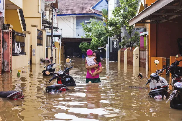 A woman carries her daughter as she wades through a flooded neighborhood in Makassar, South Sulawesi, Indonesia, Wednesday, January 23, 2019. Torrential rains that overwhelmed a dam and caused landslides killed at least six people and displaced more than 2,000 in central Indonesia, officials said Wednesday. (Photo by Yusuf Wahil/AP Photo)
