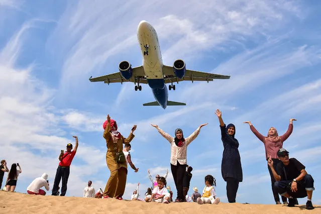 In this picture taken on February 13, 2023, tourists pose for picture on Mai Khao Beach as a plane lands at Phuket International Airport in Phuket province. (Photo by Madaree Tohlala/AFP Photo)
