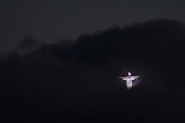 The Christ the Redeemer statue, surrounded by clouds, is lit up at dusk on June 7, 2013. (Photo by Felipe Dana/Associated Press)