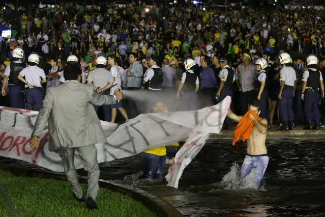 A legislative police officer sprays protesters with pepper spray to keep them from getting closer to the Congress building as demonstrators call for the impeachment of Brazil's President Dilma Rousseff and protest the naming of her mentor, former President Luiz Inacio Lula da Silva, as her new chief of staff, in Brasilia, Brazil, Wednesday, March 16, 2016. Supporters say the move will help the president fight impeachment proceedings and critics blast it as a scheme to shield Lula from possible detention in corruption probes related to a bribery scandal at Brazil's state oil company Petrobras. (Photo by Eraldo Peres/AP Photo)