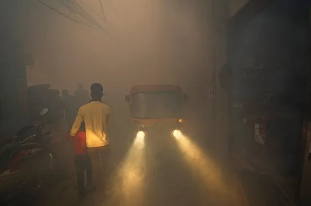 Commuters walk past smoke from fumigation in a densely populated area in New Delhi, India, Wednesday, October 27, 2021. Delhi has reported hundreds of dengue cases, with more than 200 fresh cases in the last week, according to a civic report on vector-borne diseases released on Monday. (Photo by Manish Swarup/AP Photo)