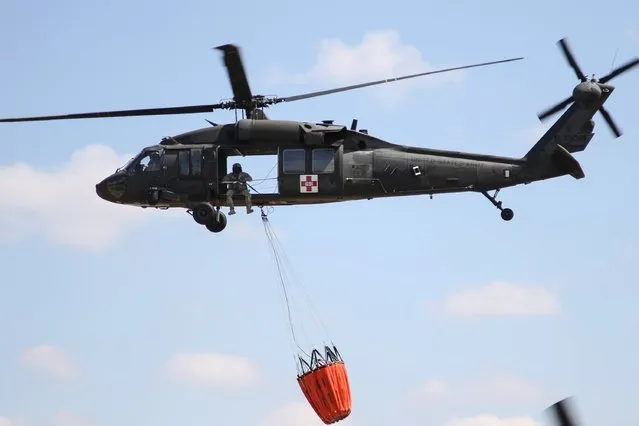 A UH-60 Black Hawk helicopter from the Kansas National Guard carries a water bucket as it prepares to help fight the Anderson Creek wildfire in southern Kansas, March 25, 2016. (Photo by Sgt. Zachary Sheely/Reuters/Kansas National Guard)