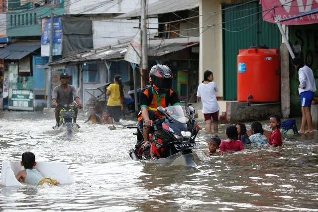 A man rides a motorbike through water, in a densely populated area that floods due to the high tides, in Muara Angke district in Jakarta, Indonesia, November 9, 2021. (Photo by Willy Kurniawan/Reuters)