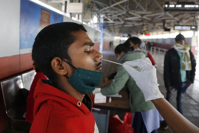 A health worker takes a swab sample of a passenger entering the city to test for COVID-19 at a railway station in Ahmedabad, India, Friday, December 3, 2021. India on Thursday confirmed its first cases of the omicron coronavirus variant in two people and officials said one arrived from South Africa and the other had no travel history. A top medical expert urged people to get vaccinated. (Photo by Ajit Solanki/AP Photo)