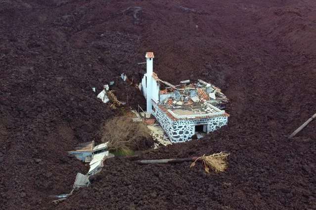 This aerial picture shows a destroyed house covered with lava following the eruption of the Cumbre Vieja volcano, in La Laguna, on the Canary Island of La Palma on December 16, 2021. A volcanic eruption on the Spanish island of La Palma has shown its first sign it might be coming to an end after nearly three months, scientists said on December 15, 2021, although they could not rule out a new flare up in activity. The eruption of the Cumbre Vieja volcano has ebbed and flowed since it first began spewing lava on September 19, forcing the evacuation of over 7,000 people and destroying nearly 3,000 buildings. (Photo by Jorge Guerrero/AFP Photo)
