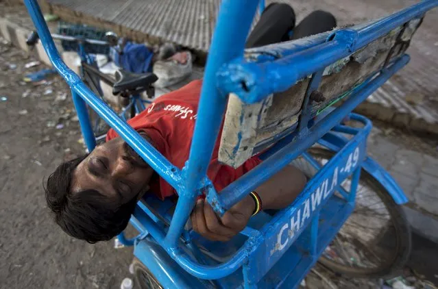 A cycle rickshaw puller sleeps on his parked rickshaw at a street in New Delhi, India, May 17, 2015. (Photo by Adnan Abidi/Reuters)