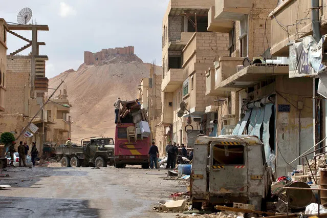 In this picture taken Thursday, April 14, 2016, the Palmyra citadel is seen in the background as Syrian families load their belongings onto a bus in the town of Palmyra in the central Homs province, Syria. (Photo by Hassan Ammar/AP Photo)
