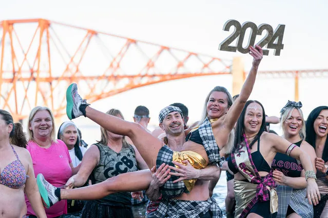 A woman holds a 2024 sign while taking part in the Loony Dook on January 1, 2024 in South Queensferry, Scotland. New Year's Day dips like the Loony Dook are a tradition in frigid waters across Britain. (Photo by Peter Summers/Getty Images)